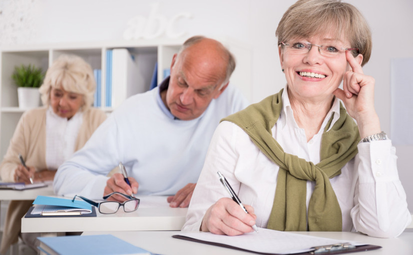 Picture senior citizen woman taking an exam in a class setting, smiling.