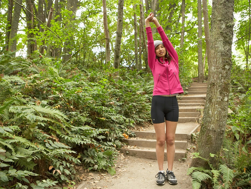 Girl stretches before a summer run on a wooded park trail.