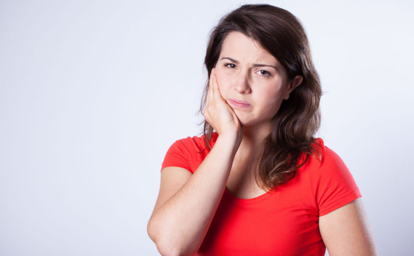 Woman with tooth pain holding her jaw with her hand.