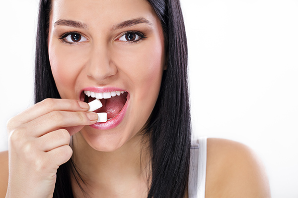 Woman placing two pieces of chewing gum in her mouth.